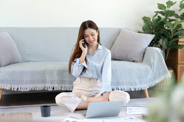 一位自由职业女性坐着用智能手机和同事聊天，用笔记本电脑打字图片下载