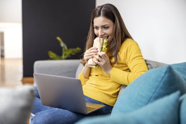女人一边吃三明治一边在笔记本电脑上工作图片下载
