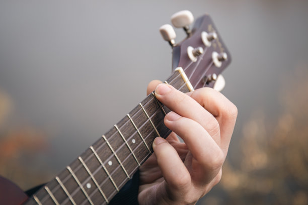 一名男子在大自然中弹奏尤克里里吉他，近距离用手指夹住琴弦。图片下载