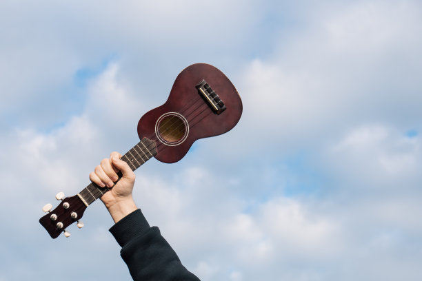 男人手中的吉他四弦琴映衬着多云的天空，自然模糊的背景。图片下载