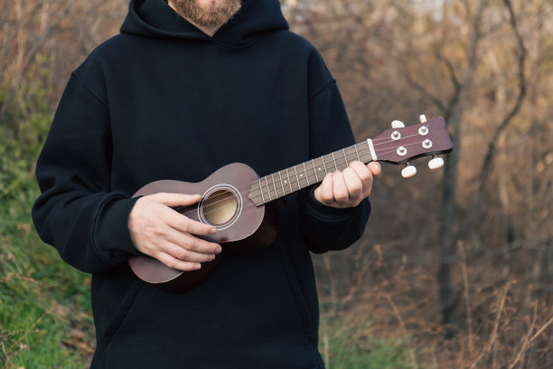 一名男子在大自然中弹着尤克里里吉他，背景模糊。图片下载