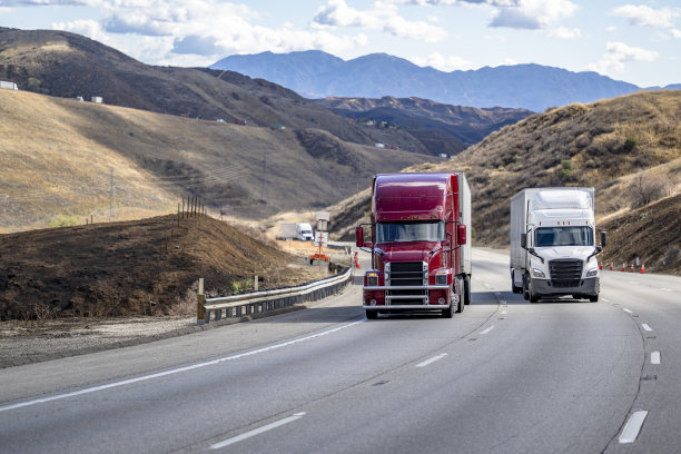 酒红色和白色的两辆不同的大卡车，带着半挂车，在蜿蜒的山路上爬坡，前往加州的山口图片下载