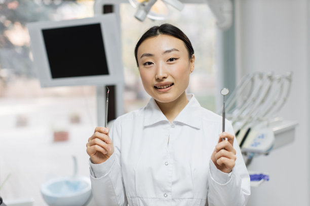 快乐的年轻女性亚洲牙医与工具站在轻现代医疗办公室的背景。图片下载