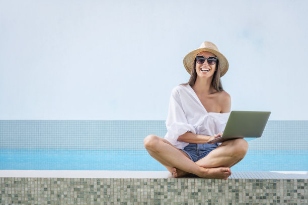 快乐的女人坐在泳池边使用她的笔记本电脑图片下载