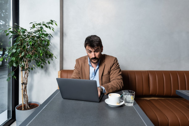 年轻成功的自雇自由职业者在自助餐厅的笔记本电脑上工作，同时喝咖啡，享受他的自由。新的小企业主从咖啡店工作图片下载