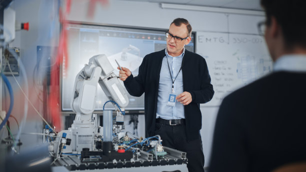 男老师在大学机器人课上与学生对话。仿生爪在讲师的监督下移动。计算机科学教育与学习概念。图片下载