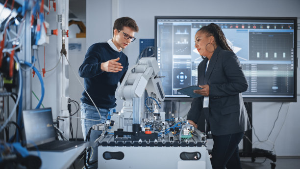 人工智能机械手的未来设计。黑人工程师向学生或创业公司讲述创新机器人手臂。先进机器人技术的工厂工作概念。缓慢的运动。图片下载