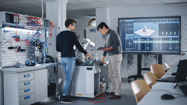 好奇的同学们在工作坊中共同研究学校工程项目中高科技机械臂的功能修改。计算机科学教育理念。图片下载