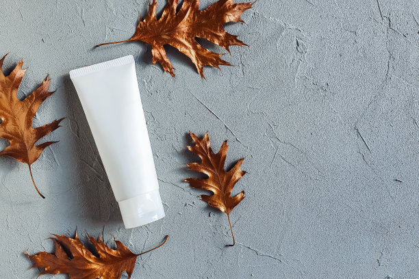 白色挤压瓶化妆品管包装和铜色橡木叶在灰色混凝土纹理背景。样品润肤霜空白瓶品牌，牙膏，护肤品，洗面奶，卸妆，凝胶图片下载