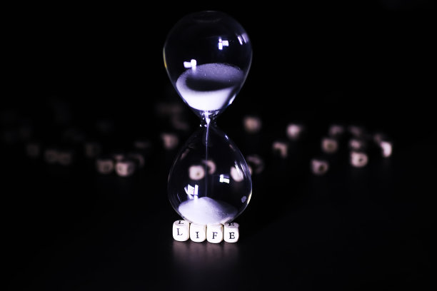 沙子穿过沙漏的灯泡，在截止日期的倒计时中测量流逝的时间，在深色的桌子背景上有复制空间。图片下载