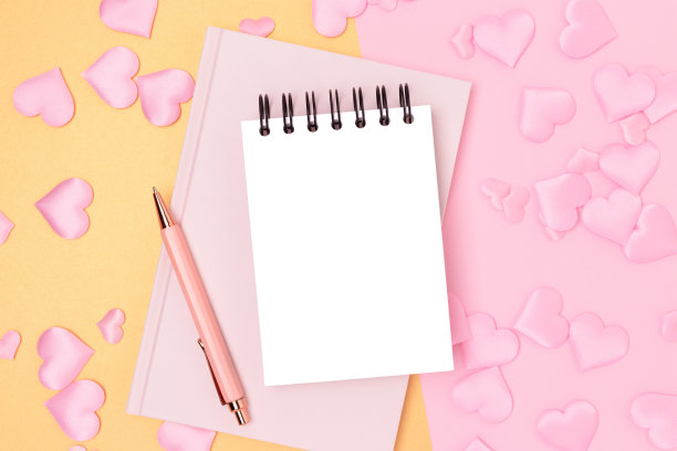 空白记事本，钢笔和粉红色背景上的纺织心形纸屑。图片下载