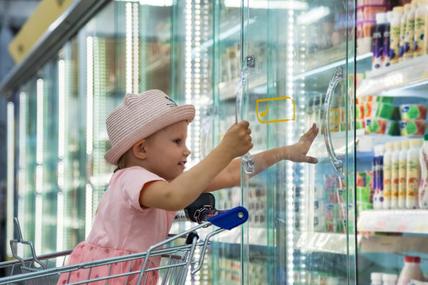 快乐的小女孩坐在食品店的购物车里，打开商店的橱窗，玩得很开心。可爱的孩子在粉红色的衣服购物和购买零售在超市。健康食品的概念。复制文本空格图片下载