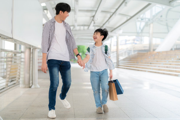 年轻的亚洲男孩拿着五颜六色的购物袋，和父亲一起走在购物中心。购物的乐趣，年终礼物的快乐。年中促销和假日概念图片下载