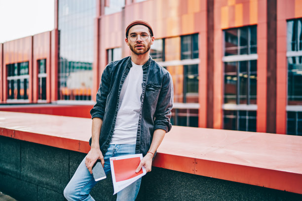 半长肖像帅气时髦的穿着男性设计师在眼镜摆造型的城市背景文件，20岁自信熟练的白人男子学生站在大学校园图片下载