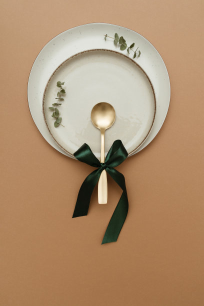 优雅的餐桌设置，两个盘子和金汤匙装饰桉树和绿色蝴蝶结。最小自然派对概念。图片下载