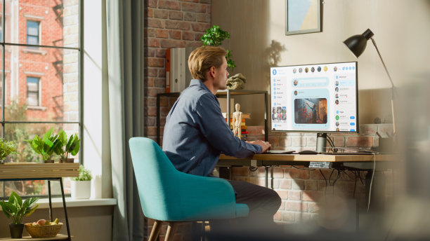 年轻英俊的男子使用台式个人电脑检查社交媒体墙Feed，直播视频，帖子，图片。模拟帖子:创意，科技，新闻，科学，生活方式内容。图片下载