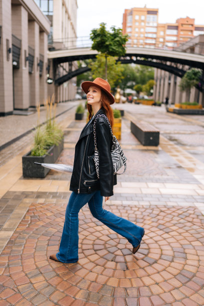 垂直全程拍摄迷人快乐的女子戴着时尚帽子走在欧洲城市的街道上，手里拿着封闭的透明伞。图片下载