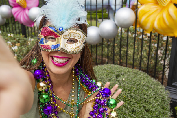 一名年轻的拉丁女游客，戴着面具，穿着服装，戴着项链，在新奥尔良的街道上庆祝狂欢节，同时用她的手机自拍。图片下载