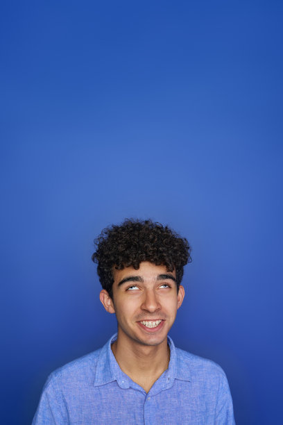 有趣的年轻男性，卷发微笑着，在蓝色背景下做鬼脸和滚动眼球图片下载