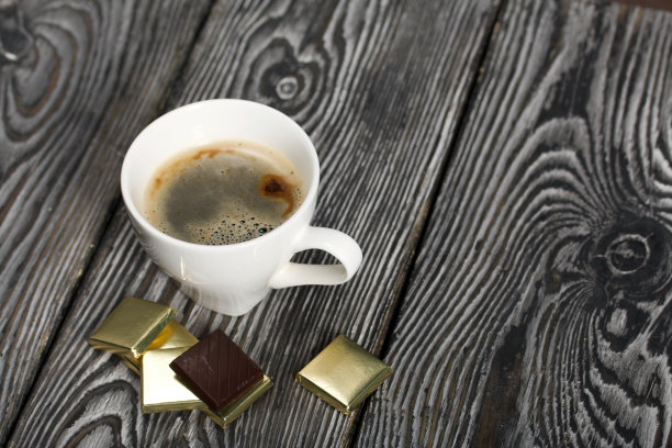 一杯白杯子里的黑咖啡。铝箔巧克力。在松木板上。图片下载