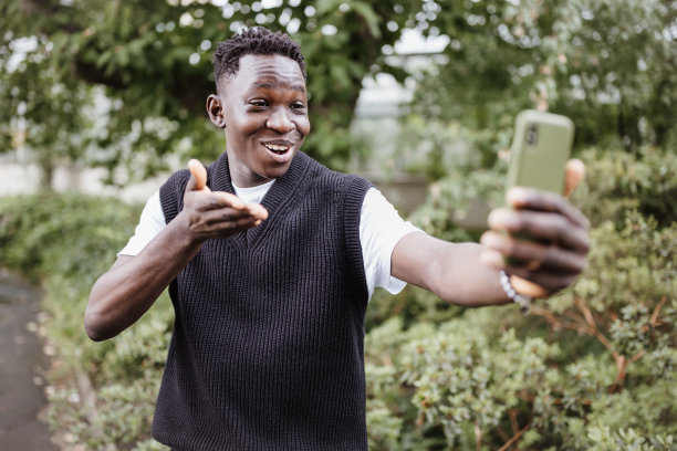 年轻的非洲男子在公园里微笑着用手机自拍或拍视频图片下载