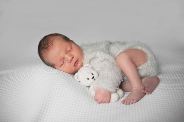 刚出生10天的婴儿穿着针织工作服和熊玩具睡在白色背景上图片下载
