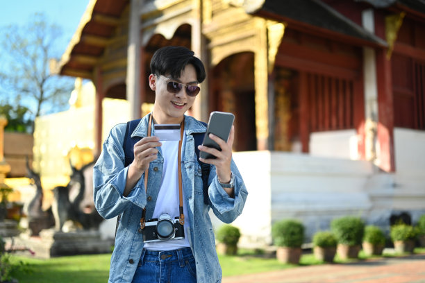 在泰国度假时，快乐的男子旅行者手拿智能手机和信用卡。图片下载
