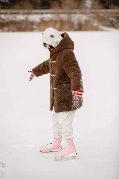 孩子们在冰湖上滑冰，在雪林里。在寒冷的冬天，小女孩穿着温暖的衣服和粉红色的冰鞋在天然冰面上溜冰场。假期快乐图片下载