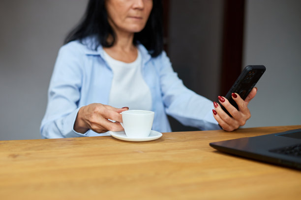 年长的女商人在工作场所放松，使用手机图片下载