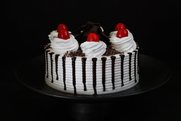 黑色森林奶油蛋糕的图片，上面点缀着鲜奶油莲座，上面是莫雷罗樱桃，豪华的巧克力蛋糕上涂着鲜奶油，上面覆盖着融化的巧克力，黑色背景图片下载