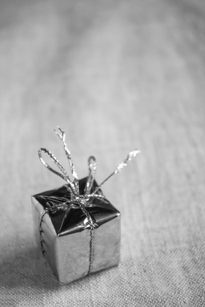 桌上有一份礼物。装着礼物的盒子装在一个闪亮的包装里，用丝带系着。桌上有一份礼物。灰色色调极简主义的礼物。图片下载
