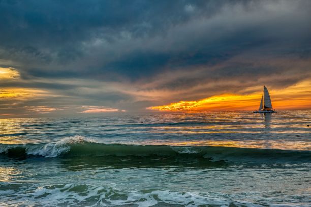 日落时分，大海中帆船的海浪美景图片下载