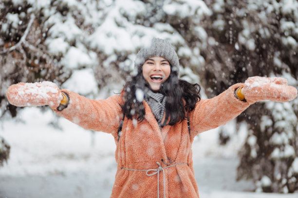 迷人的年轻女子在一个温暖的粉红色外套有乐趣，微笑和小跑一个覆盖着雪的树枝和雪落在上面。冬季娱乐图片下载