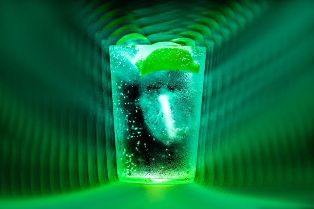 一大杯杜松子酒加奎宁水，加冰的奎宁汽水和一片迷幻绿色背景的柠檬图片下载