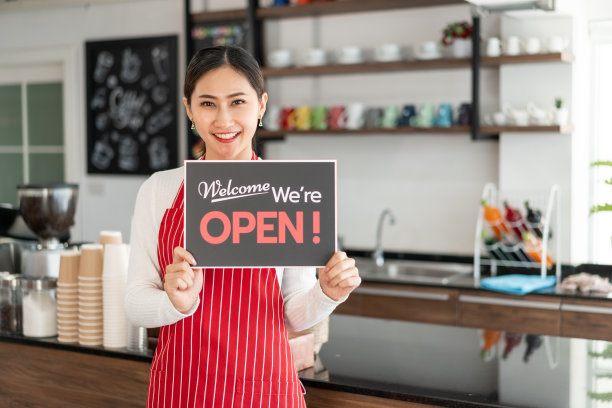 女老板站在她的咖啡店门口的肖像，显示打开的招牌图片下载