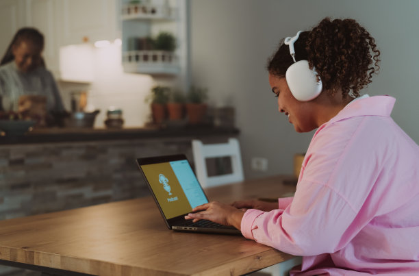 年轻的非洲女孩使用笔记本电脑听播客，而她的母亲在家里做饭的背景图片下载