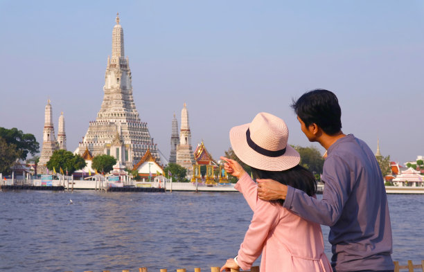 一对情侣在泰国曼谷朝湄南河岸边的著名地标——黎明寺的标志性佛塔图片下载