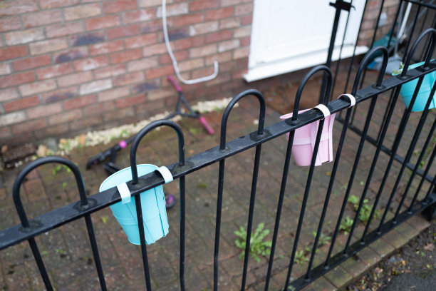 一幢屋苑前花园的栅栏上悬挂着五颜六色的金属植物桶。图片下载