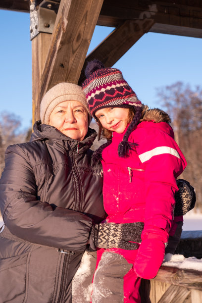 一个77岁的老妇人，一个7岁的女孩，拥抱着爱和温柔。奶奶和孙女在冬天一起散步。图片下载