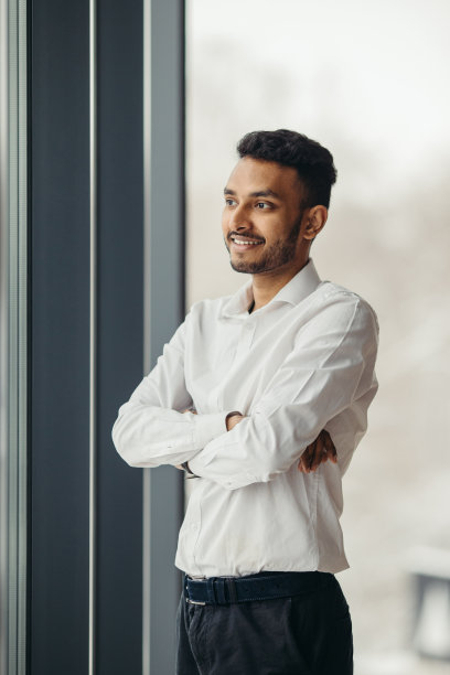 年轻的印度商人在办公室的窗户附近摆姿势。图片下载