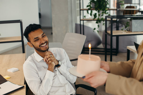一名年轻的印度男子正准备吹灭蛋糕上的蜡烛，并在与同事的生日庆祝活动中许愿。同事们在办公室庆祝生日图片下载