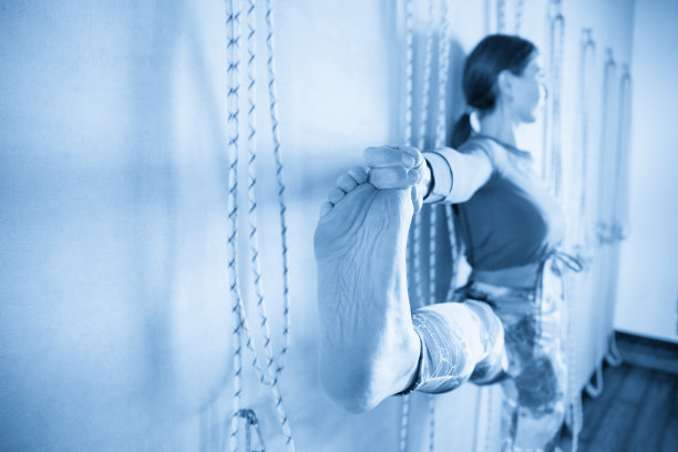 年轻女孩做瑜伽姿势，她的脚趾站在墙上用绳子图片下载