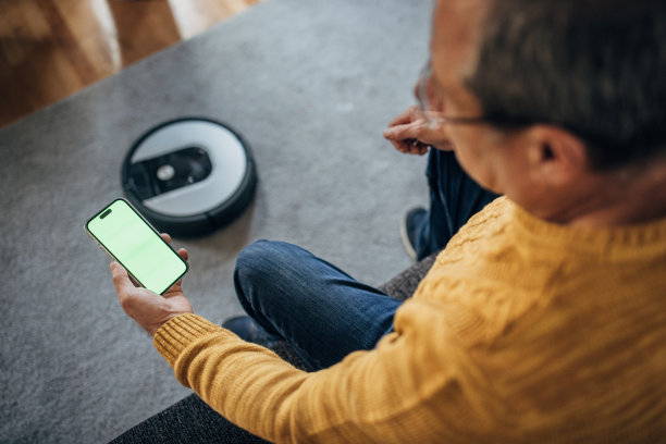 一位老年人使用机器人吸尘器和智能手机图片下载