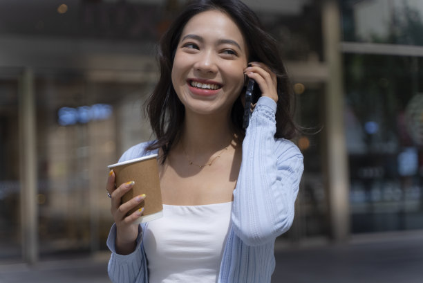 快乐的年轻亚洲女子在城市里打电话图片下载