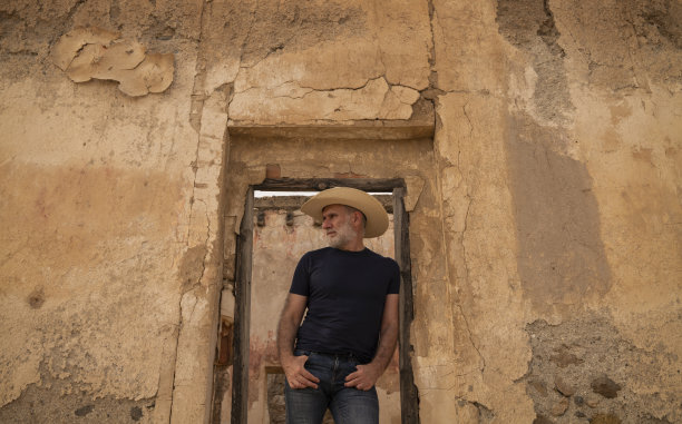 戴牛仔帽的成年男子站在废弃建筑的门口图片下载