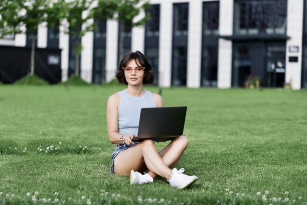 美丽的微笑女孩在公园里用笔记本电脑工作图片下载