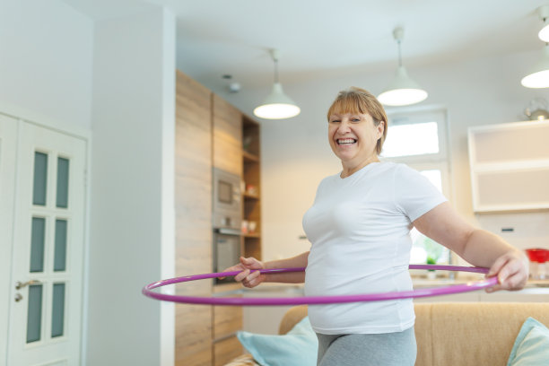 穿着白色t恤和灰色紧身裤的超重成熟女子试图用呼啦圈练习减肥图片下载