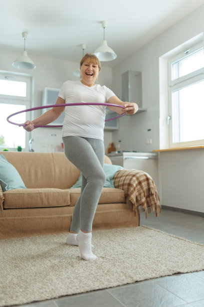 穿着白色t恤和灰色紧身裤的超重成熟女子试图用呼啦圈练习减肥图片下载