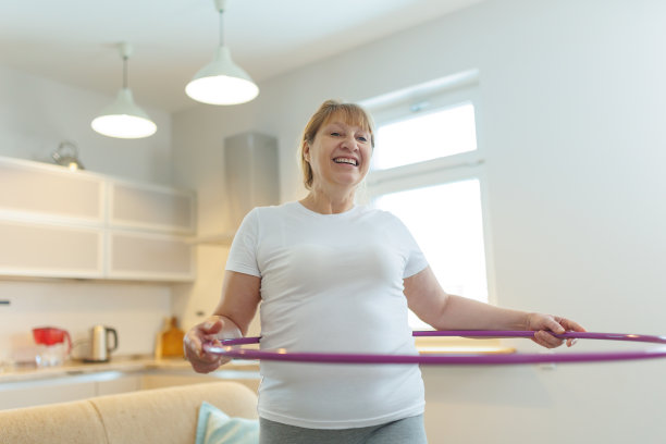 穿着白色t恤和灰色紧身裤的超重成熟女子试图用呼啦圈练习减肥图片下载