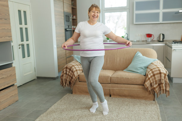 穿着白色t恤和灰色紧身裤的超重成熟女子试图用呼啦圈练习减肥图片下载